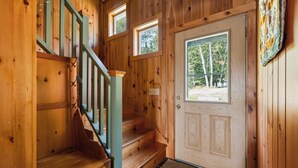 Un escalier en bois menant à une porte dotée d’une fenêtre, un paillasson et une courtepointe accrochée au mur.