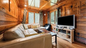 L’intérieur d’un chalet en bois comprend un canapé, un téléviseur et un meuble de rangement en osier.