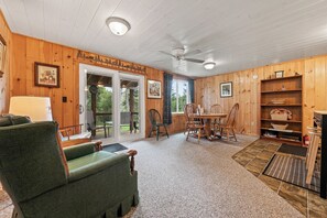 A cozy cabin interior with a green armchair, a dining table with chairs, a fireplace, and a bookshelf. - Pine Valley - Great newly renovated cabin - close to the village of Oquossoc (Rangeley)
