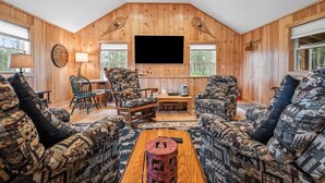 Un salon chaleureux avec des murs en bois, un grand téléviseur à écran plat, des meubles à motifs et une cheminée.