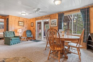 A cozy cabin interior with a dining area, a green armchair, and a ceiling fan.