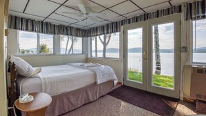 Ein Schlafzimmer mit Bett, Nachttisch, Deckenventilator, Fenster mit Seeblick und einer Tür, die nach draußen führt.