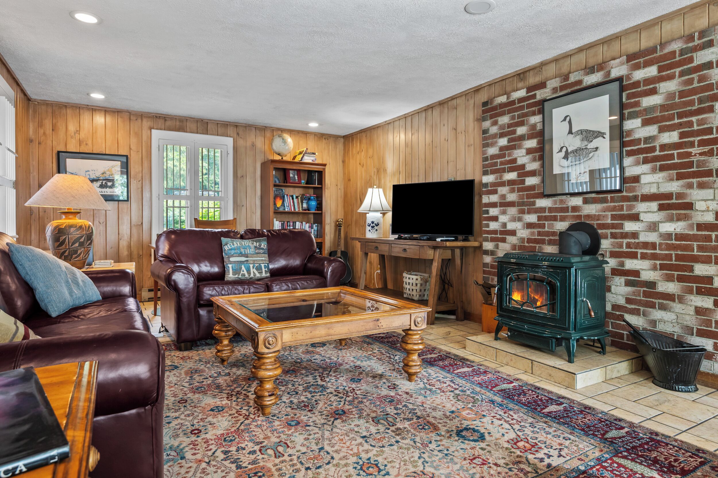 A cozy living room with leather sofas, a glass coffee table, a fireplace, and a bookshelf.
