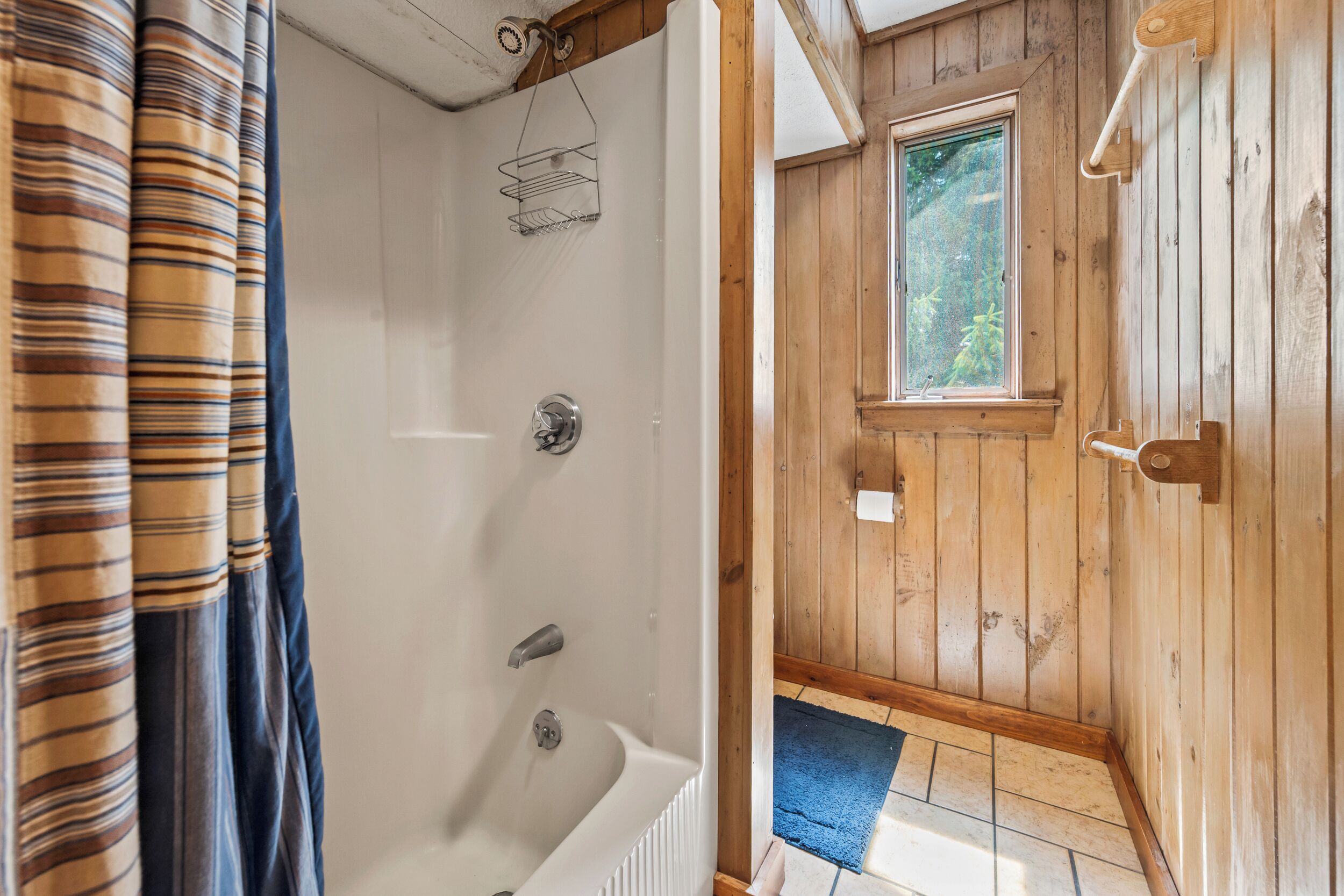 Une salle de bain rustique, avec des murs en bois, comprenant une baignoire, une douche et une fenêtre.