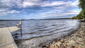 A rocky shoreline with a wooden dock and a chair.