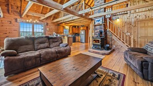 A log cabin interior with a wooden ceiling, a fireplace, a sofa, and a dining table. - 🐾33 Loop Rd Log Cabin w/ Shared Rangeley Lake Access, Snowmobile/ATV Access, 15 min to Saddleback (Rangeley)