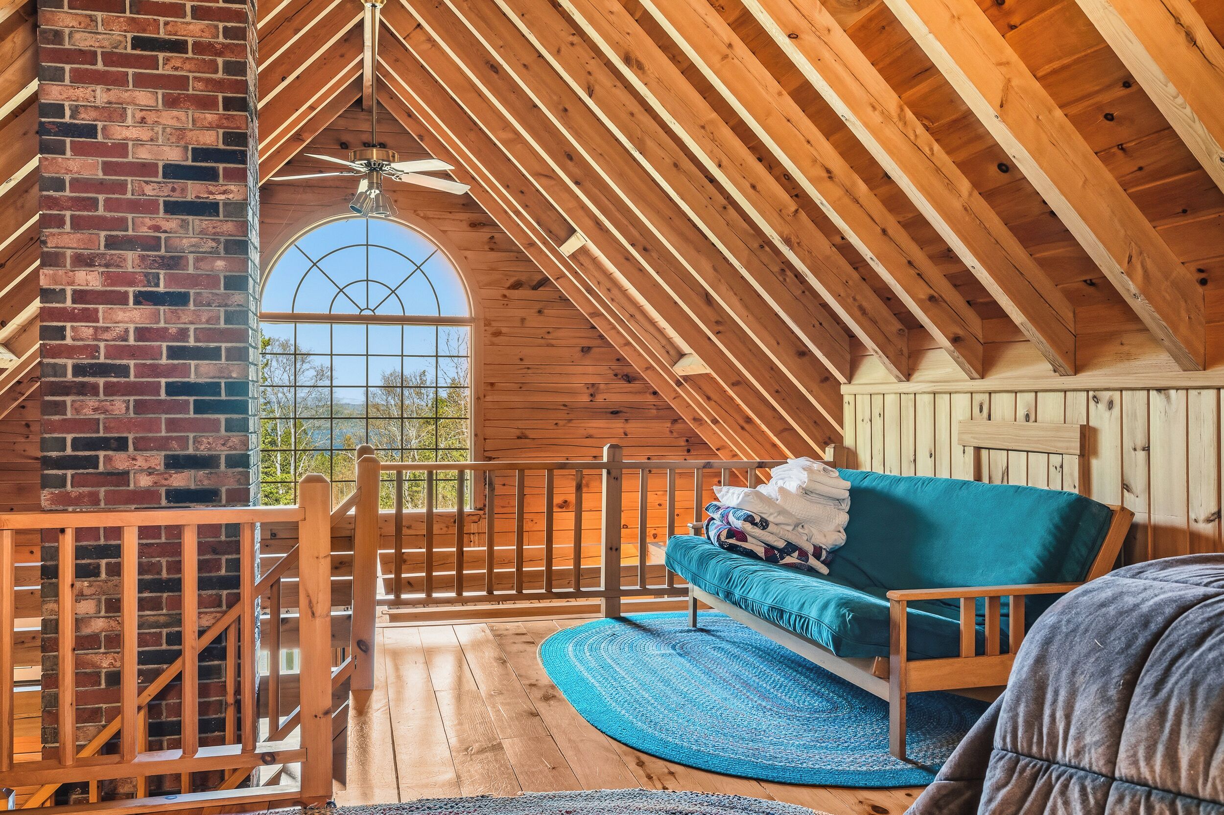 Ein Schlafzimmer im Loft-Stil mit Holzbalkendecke, Backsteinwand, einem großen Bogenfenster, einem hölzernen Bett und einem blauen Teppich.