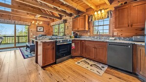 A wooden cabin kitchen with a large window, wooden ceiling beams, and a built-in oven. - 🐾33 Loop Rd Log Cabin w/ Shared Rangeley Lake Access, Snowmobile/ATV Access, 15 min to Saddleback (Rangeley)