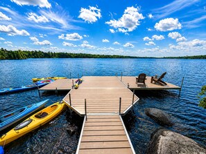 Eine Holzsteganlage, die sich in einen ruhigen See erstreckt, mit angedockten Kajaks und einem Stand-Up-Paddleboard.