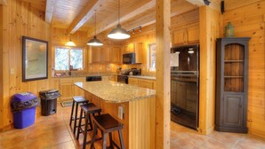 Une cuisine rustique aménagée dans une cabane en bois, dotée de plans de travail en granit, d’un réfrigérateur et d’un coin bar.