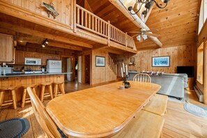 A wooden cabin interior with a dining area, kitchen, and a balcony.