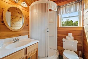 A wooden cabin bathroom with a sink, toilet, and shower.