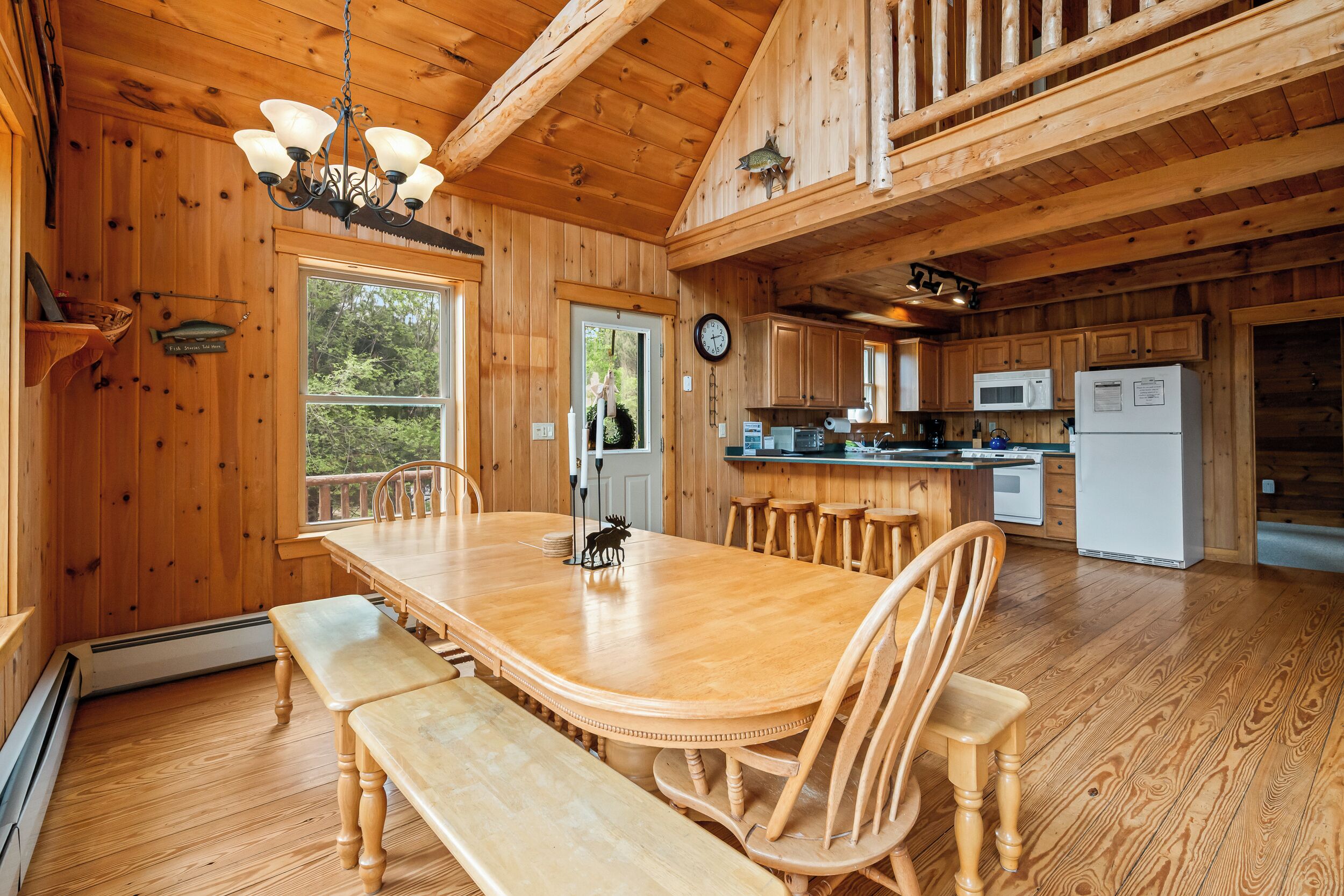 Una cabaña de madera con comedor, cocina y un amplio ventanal.
