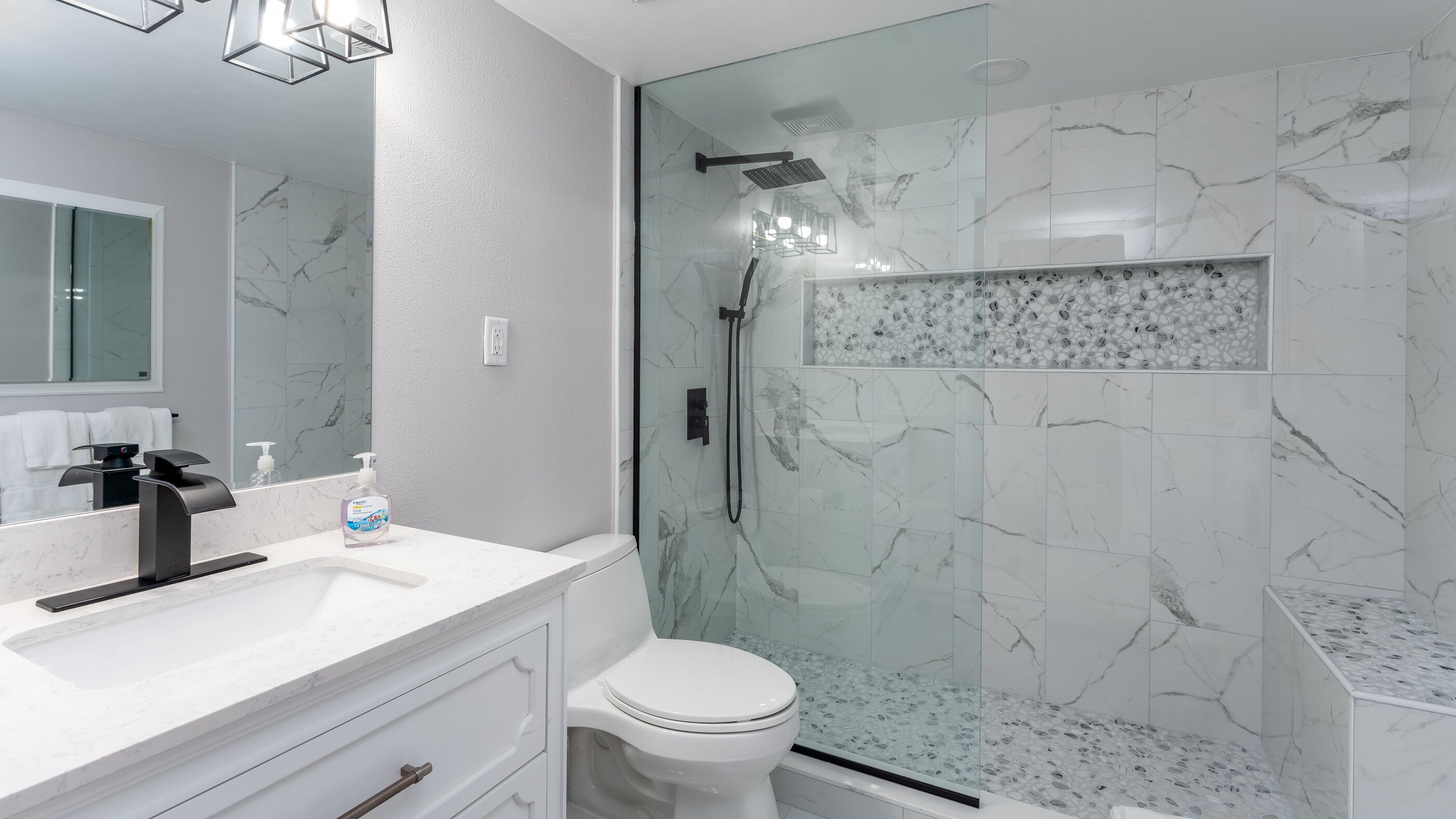 A modern bathroom with a glass-enclosed shower, a white toilet, and a marble-tiled vanity.