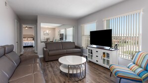 Een moderne woonkamer met een bank, een ronde tafel, een televisie en een kleurrijke fauteuil.