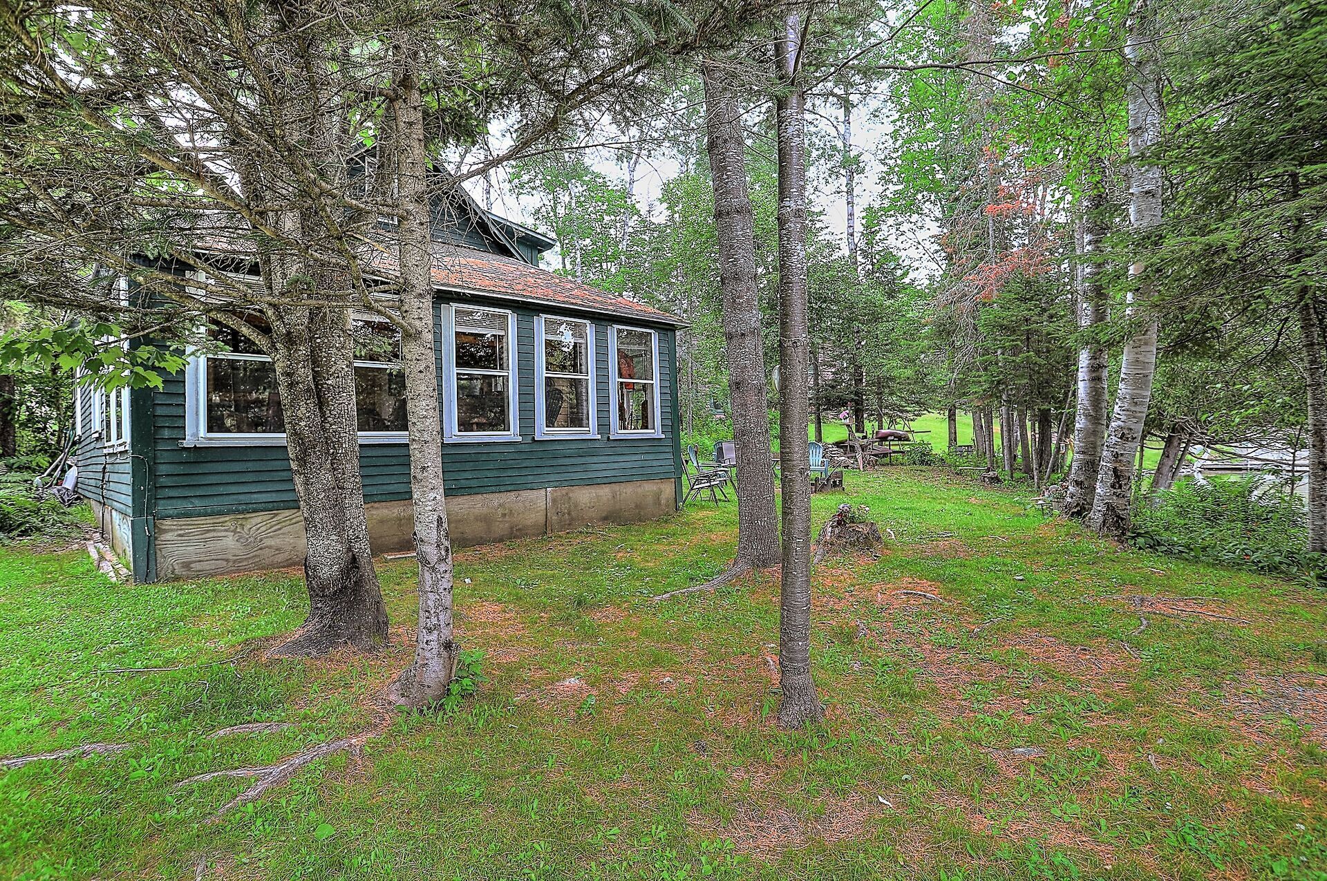 Une petite cabane à un seul étage, à l’extérieur vert, entourée d’une zone boisée.