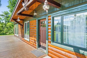 Une cabane en rondins avec une terrasse en bois, de grandes fenêtres et une porte.