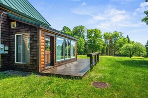 A log cabin with a deck, large windows, and a green roof.