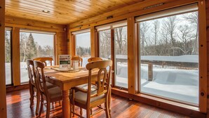 Un interior de madera con una mesa de comedor y sillas, ventanas amplias y vistas a un paisaje nevado.