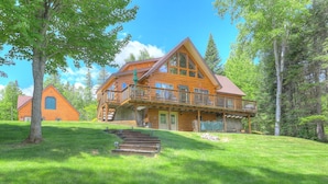 A log cabin with a balcony, surrounded by lush greenery and trees.