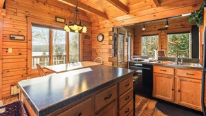 A wooden cabin interior with a kitchen area featuring a granite countertop, wooden cabinets, a sink, and a refrigerator.