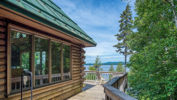 Une cabane en rondins dotée d’une terrasse offrant une vue sur un lac et des montagnes.