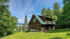 Une cabane en bois avec un toit vert, entourée d’une végétation luxuriante et offrant une vue sur un lac.