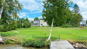 A riverside park with a wooden dock, grassy areas, and houses in the background. - Village Walk | Convenient & Charming, Hot tub (Rangeley)