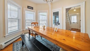 A dining area with a wooden table, benches, and a chandelier. - Village Walk | Convenient & Charming, Hot tub (Rangeley)