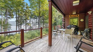 A wooden deck with outdoor furniture, a grill, and a view of a lake surrounded by trees.