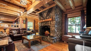 A cozy log cabin interior with a stone fireplace, leather furniture, and wooden floors.