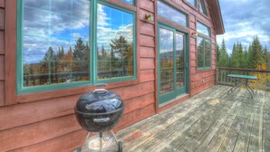 A wooden cabin with large windows, a barbecue grill, and a deck with a table and chairs. - Reid - Private cabin with Rangeley Lake access! (Rangeley)