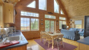 A cabin with a kitchen, dining area, and living room, featuring large windows and wooden interiors. - Reid - Private cabin with Rangeley Lake access! (Rangeley)