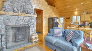 A cozy cabin interior with a stone fireplace, a blue sofa with striped pillows, and a wooden dining area. - Reid - Private cabin with Rangeley Lake access! (Rangeley)