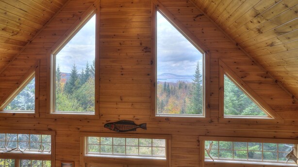 A cabin with a high, sloped wooden roof and multiple windows offering views of a forested landscape. - Reid - Private cabin with Rangeley Lake access! (Rangeley)