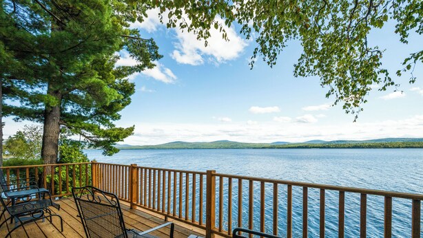 Eine Holzterrasse mit Metallstühlen und -tischen mit Blick auf einen See.