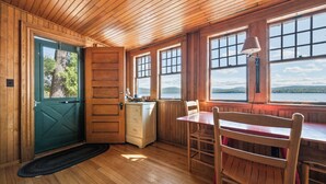 Ein Holzinterieur mit einem Esstisch und Stühlen, einem Fenster mit Blick ins Freie und einer Tür mit Fenster.