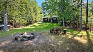 A cabin with a fire pit and picnic table in a forested area. - CedarDuft Cottage - Cozy log cabin right on the shores of Quimby Pond (Rangeley)