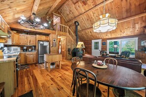 A wooden cabin interior with a kitchen, dining area, and a loft bedroom.
