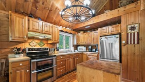 A wooden cabin-style kitchen with a central island, stainless steel appliances, and a hanging light fixture. - CedarDuft Cottage - Cozy log cabin right on the shores of Quimby Pond (Rangeley)
