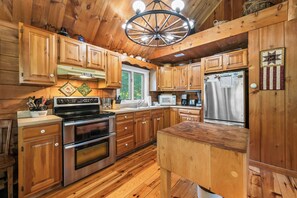 Une cuisine de style rustique, avec des éléments en bois, un îlot central, des appareils en acier inoxydable et un luminaire suspendu.