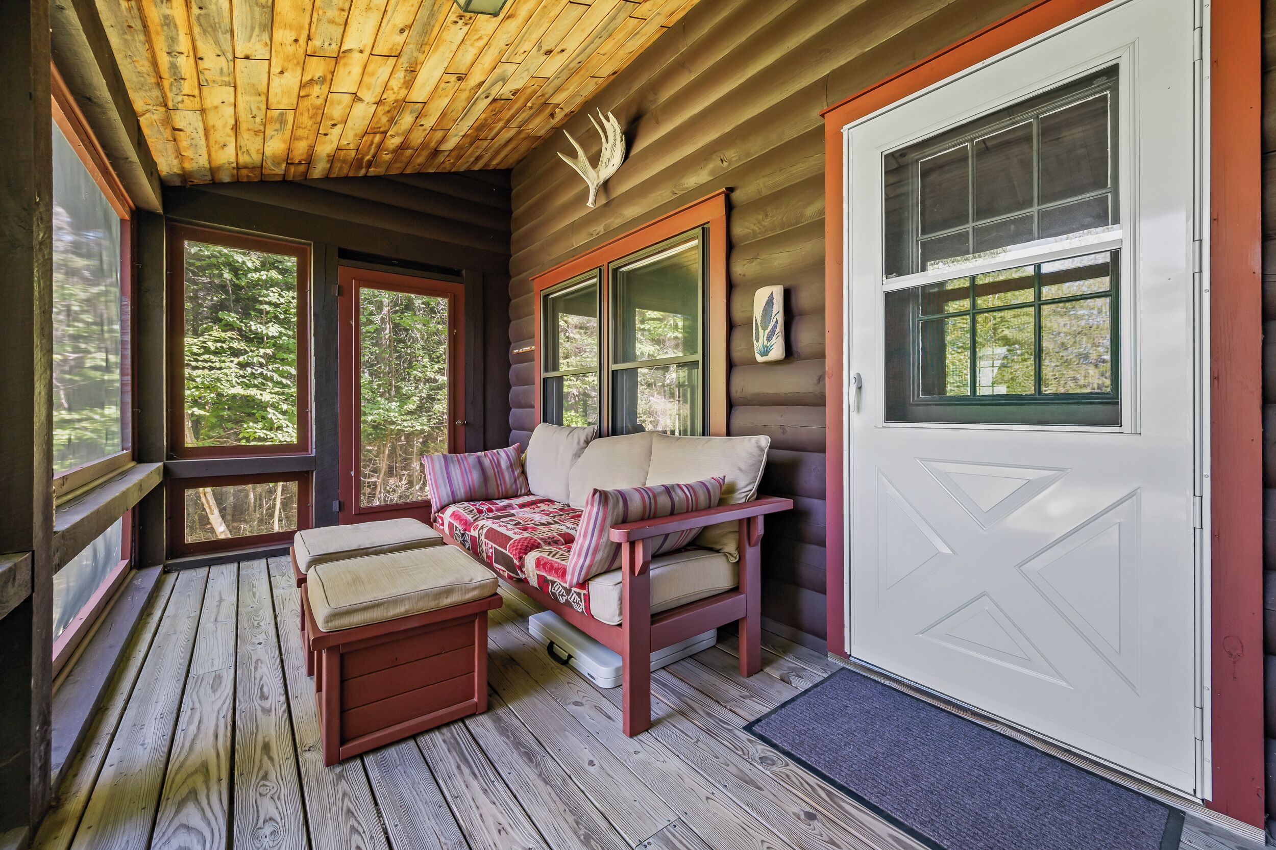 A cozy cabin interior with a wooden deck, a cushioned bench, and a door with a window.