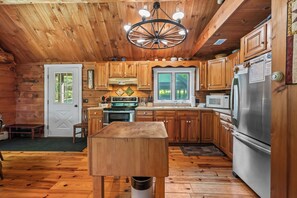 A wooden cabin kitchen with a central island, wooden cabinets, a stainless steel refrigerator, and a chandelier.