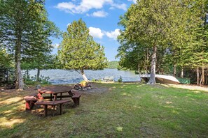 Ein Picknickplatz am Seeufer mit Holztisch und Bänken, umgeben von Bäumen und Blick auf den See.