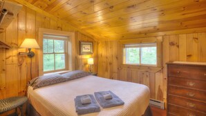 Ein Schlafzimmer in einer Holzhütte mit einem Bett, zwei Fenstern, einem Schminktisch und Wandlampen.