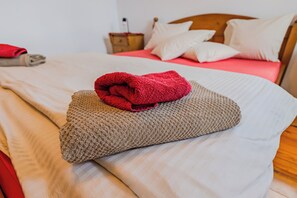 Cama bem arrumada com uma toalha vermelha e um travesseiro bege.