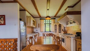 A kitchen with a wooden dining table, cabinets, and a window with curtains.