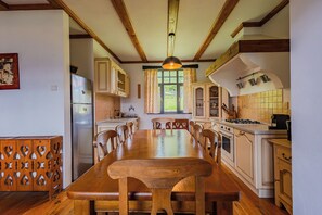 Cozinha com mesa de jantar de madeira, armários e janela com cortinas.