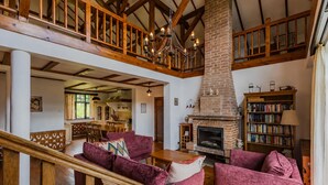 A spacious living area with a fireplace, wooden staircase, and a high ceiling.