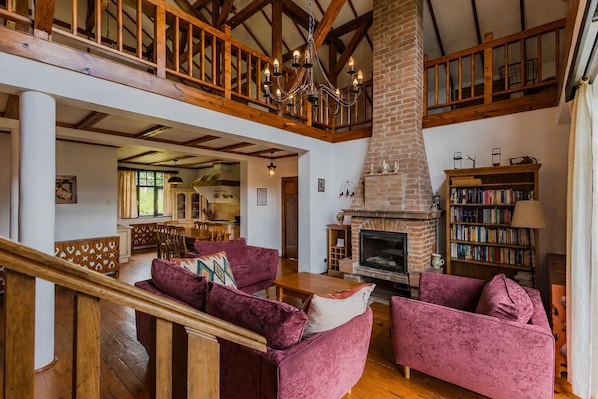 A spacious living area with a fireplace, wooden staircase, and a high ceiling.